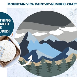 Peut inclure: Un kit de peinture par num&eacute;ros repr&eacute;sentant un paysage de montagne avec une palette de couleurs bleue, grise et blanche. Le kit comprend une toile en bois, des pots de peinture et des pinceaux. Le texte "Tout ce dont vous avez besoin est inclus !" est affich&eacute; dans un cercle bleu.