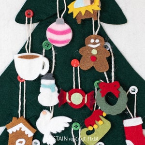 May include: A felt Christmas tree with various felt ornaments hanging from it. The ornaments include a gingerbread man, a candy cane, a snowman, a dove, a stocking, a coffee cup, a wreath, a star, a gingerbread house, and a nativity scene.