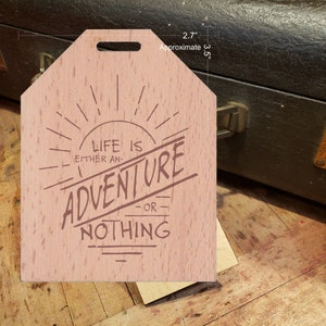 May include: A light brown wooden sign with the text "LIFE IS EITHER AN ADVENTURE OR NOTHING" in a stylized font. The sign is approximately 3.5 inches tall and 2.7 inches wide, with a small hole at the top for hanging.