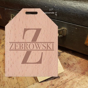 May include: A wooden luggage tag with a light brown finish. The tag has a cut-out handle and is engraved with the letter "Z" and the name "ZEBROWSKI". The tag measures approximately 2.7 inches by 3.5 inches.