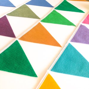 May include: A colorful felt banner with alternating triangles in shades of green, purple, orange, blue, and teal. The banner is strung on a white cord.