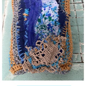 Könnte beinhalten: Handgefertigte Patchwork-Tasche in Blau-, Braun- und Grautönen. Die Tasche hat verschiedene Stoffe, darunter Blumenmuster und Häkeldetails. Der Text "SUMMER MEMORIES WOOLEN ART" ist unten im Bild zu sehen.