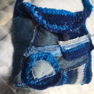 Könnte beinhalten: Eine kleine blaue Patchwork-Tasche aus Jeans und blauem Stoff mit blauem Häkelrand.
