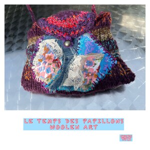 以下が含まれることがあります： 花柄の生地とデニムを使ったパッチワークのデザインが施された、小さな紫色の編み物バッグ。バッグはボタン留めとストラップが付いています。バッグの下には「LE TEMPS DES PAPILLONS WOOLEN ART」という文字が印刷されています。