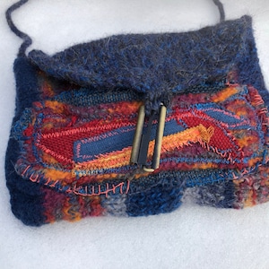Könnte beinhalten: Eine kleine blaue Stricktasche mit einer Klappe und einem bunten Patchwork-Design. Die Tasche hat einen Metallverschluss und einen langen Riemen.