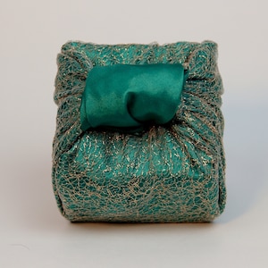 Puede incluir: Una caja de regalo verde con un patrón metálico dorado y un lazo de satén verde.