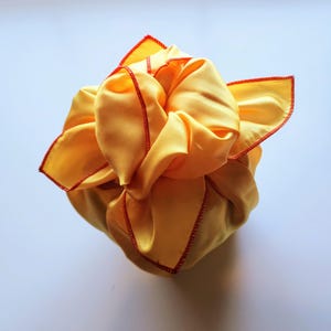 May include: A yellow fabric gift wrap with red stitching. The fabric is tied in a knot and the ends are tucked in.