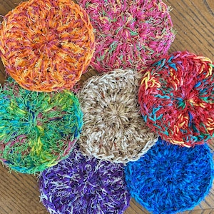 May include: Six colorful crocheted scrubbers in various colors, including orange, pink, green, brown, purple, and blue. The scrubbers are made of a soft, textured material and are perfect for cleaning dishes or other surfaces.