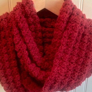 May include: A red crocheted infinity scarf. The scarf is made with a textured stitch that gives it a puffy look.