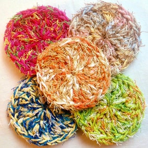 May include: Five colorful crocheted scrubbers in various shades of pink, blue, green, yellow, and orange. The scrubbers are made of yarn and have a fluffy texture.
