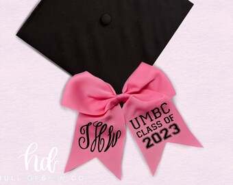 May include: Pink graduation bow with black text that says "UMBC Class of 2023" and a black monogram that says "JFF".