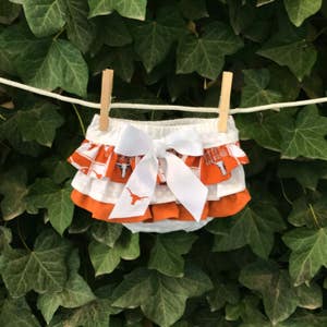 May include: White and orange baby bloomers with a white bow and a Texas Longhorns logo print.