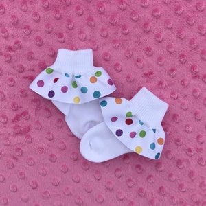 May include: Two pairs of white baby socks with a colorful polka dot ruffle trim.