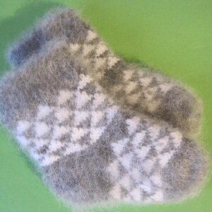 May include: A pair of gray and white knitted baby socks. The socks have a soft, fuzzy texture and a geometric pattern in white. The background is a solid green.