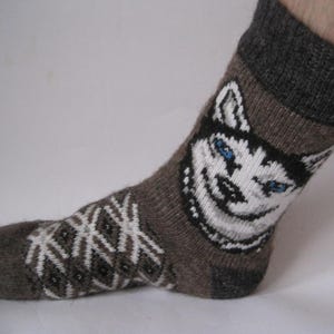 May include: Brown wool socks with a white husky face design and a geometric pattern on the foot. The socks have a gray cuff.