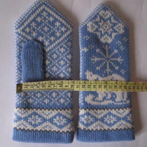 May include: A pair of blue and white knitted mittens with a geometric and snowflake pattern. The mittens measure approximately 9 inches in length. The thumb is a solid blue color.