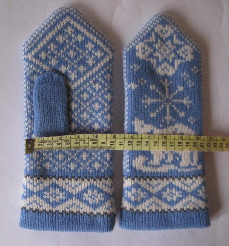 May include: A pair of blue and white knitted mittens with a geometric and snowflake pattern. The mittens measure approximately 9 inches in length. The thumb is a solid blue color.