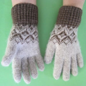 May include: A pair of knitted gloves with a brown cuff and a light gray body. The gloves feature a geometric diamond pattern in brown on the back of the hand. The gloves are made of a soft, fuzzy material.