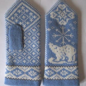 May include: A pair of light blue knitted mittens with white and gray geometric patterns. One mitten features a polar bear and snowflake design. The mittens are made of a soft, warm material, perfect for cold weather.