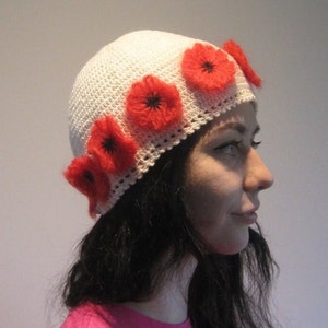 May include: A white crocheted hat with a band of red felt poppy flowers.