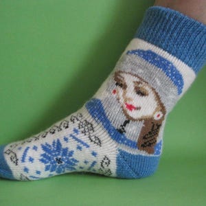 Puede incluir: Calcetines blancos y azules con un puño azul y una cara de mujer de dibujos animados en la parte delantera.