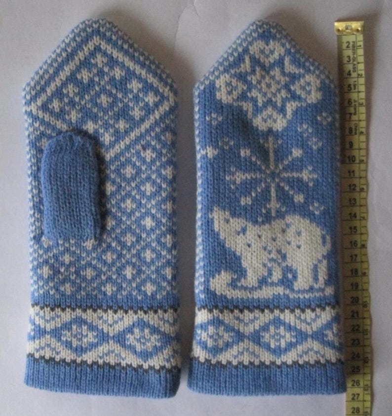 May include: A pair of blue and white knitted mittens. One mitten features a polar bear design, while the other has a geometric pattern. The mittens are approximately 10 inches long.
