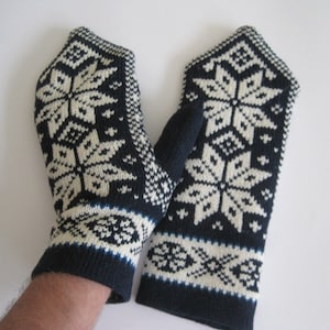 Könnte beinhalten: Ein Paar schwarze und weiße Strickhandschuhe mit einem Schneeflockenmuster. Die Handschuhe haben einen blauen Saum.