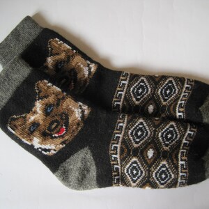 May include: A pair of black wool socks with a brown and white geometric pattern and a cartoon dog face on each sock.