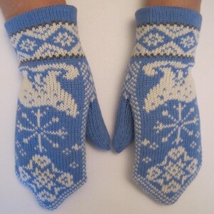 May include: A pair of light blue knitted mittens with white and dark grey geometric and snowflake patterns. The mittens have a thumb and are designed for warmth and winter wear.