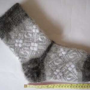 K&ouml;nnte beinhalten: Ein flauschiger, wadenhoher Socken mit einem grau-wei&szlig;en geometrischen Rautenmuster. Der Socken hat ein dunkelgraues B&uuml;ndchen sowie eine dunkelgraue Ferse und Spitze. Ein gelbes Ma&szlig;band liegt darunter und zeigt eine L&auml;nge von etwa 28 cm.