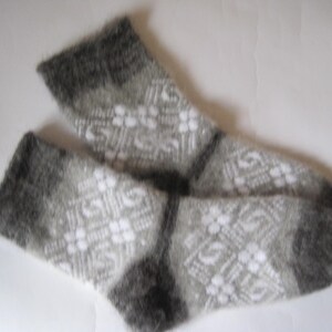 K&ouml;nnte beinhalten: Ein Paar flauschige wadenhohe Socken mit einem geometrischen Muster in Grau und Wei&szlig;. Die Socken haben eine weiche, geb&uuml;rstete Textur mit einfarbigen dunkelgrauen B&uuml;ndchen, Fersen und Zehen, kontrastiert durch ein komplexes Rautenmuster.