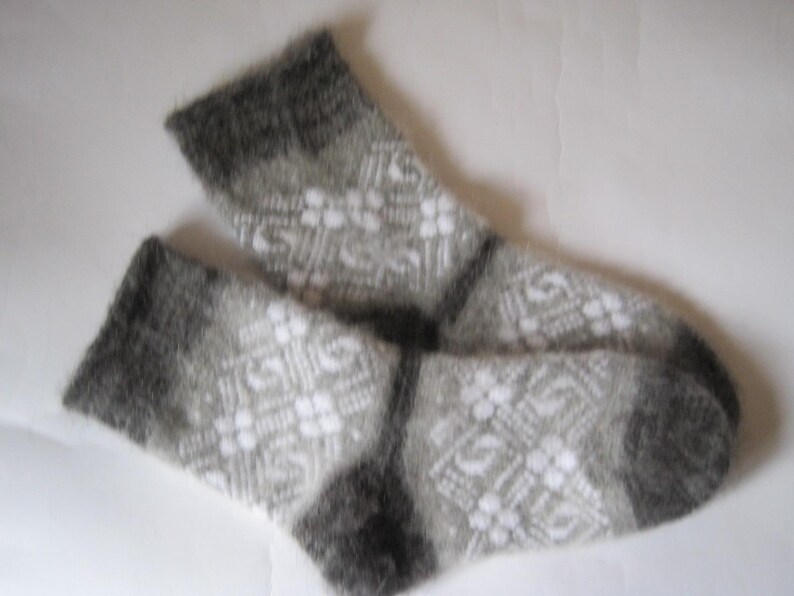 K&ouml;nnte beinhalten: Ein Paar flauschige wadenhohe Socken mit einem geometrischen Muster in Grau und Wei&szlig;. Die Socken haben eine weiche, geb&uuml;rstete Textur mit einfarbigen dunkelgrauen B&uuml;ndchen, Fersen und Zehen, kontrastiert durch ein komplexes Rautenmuster.