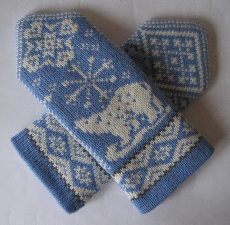 May include: A pair of light blue knitted mittens with white snowflake and animal patterns. The mittens have a cuff with a geometric design. The mittens are designed for cold weather and are made of a soft, warm material.