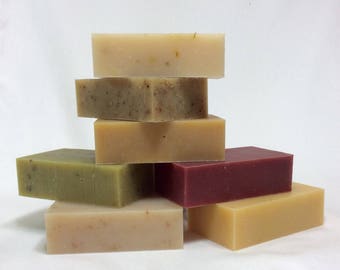 May include: A stack of six handmade soap bars in various colors and textures. The bars are arranged in a pyramid shape, with the largest bar at the bottom and the smallest bar at the top. The bars are made with natural ingredients and are free of harsh chemicals.