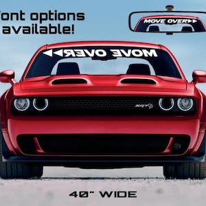 Könnte beinhalten: Ein roter Dodge Challenger SRT mit einem schwarzen "MOVE OVER" Aufkleber auf der Windschutzscheibe. Der Aufkleber ist 40 Zoll breit. Das Auto steht auf einem Feldweg.