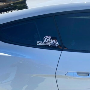 May include: A white vinyl decal applied to the rear side window of a silver car. The decal features a stylized Instagram camera icon positioned above the text "yss_molly5oh" in a bold, sans-serif font with a thick white outline and black fill.