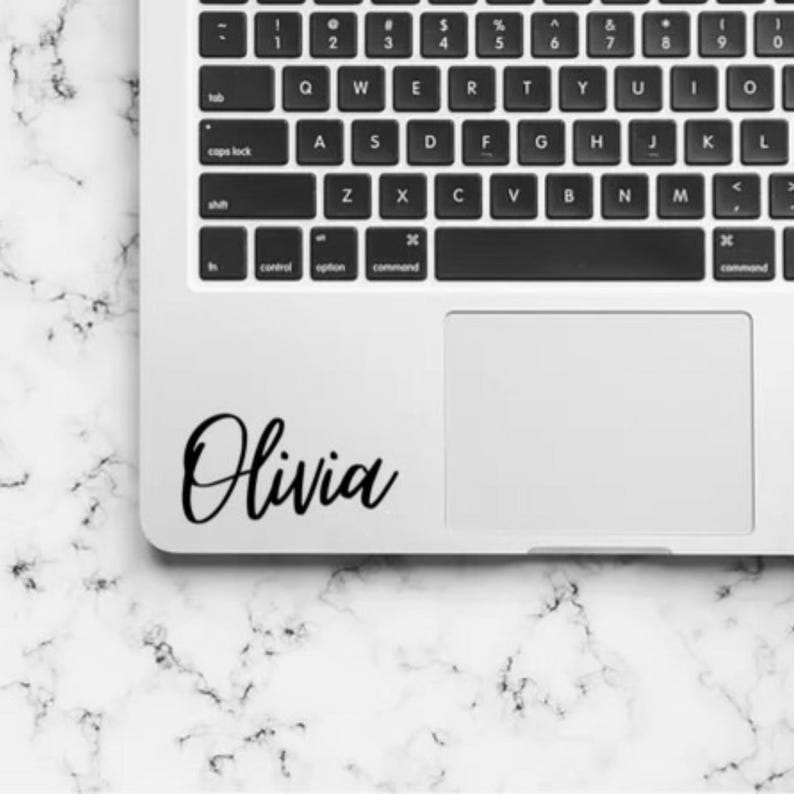 Pu&ograve; includere: Un portatile color argento con tastiera QWERTY nera e trackpad. Un adesivo in vinile nero con il nome Olivia in un carattere corsivo &egrave; applicato nell'angolo inferiore sinistro della scocca del portatile, sotto la tastiera e a sinistra del trackpad.