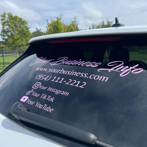以下が含まれることがあります： ピンクと白の車の窓用ステッカーで、「Your Business Info」というテキストとウェブサイトアドレス「www.yourbusiness.com」が書かれています。ステッカーには、電話番号、ソーシャルメディアのハンドル、Instagram、TikTok、YouTubeのアイコンも含まれています。