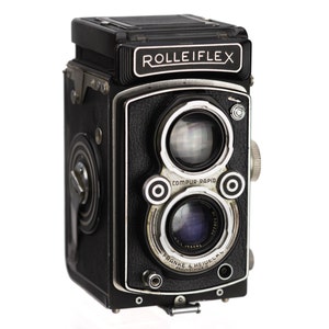 May include: A black Rolleiflex twin-lens reflex camera with a silver lens and the text "COMPUR-RAPID" and "FRANK & HEIDEKEAN" printed on the front.