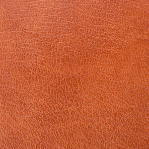 Puede incluir: Primer plano de una superficie de cuero texturizado, marr&oacute;n anaranjado. El cuero tiene un patr&oacute;n fino y agrietado, creando una apariencia detallada y t&aacute;ctil. El color es un tono c&aacute;lido y terroso, lo que sugiere un material natural.
