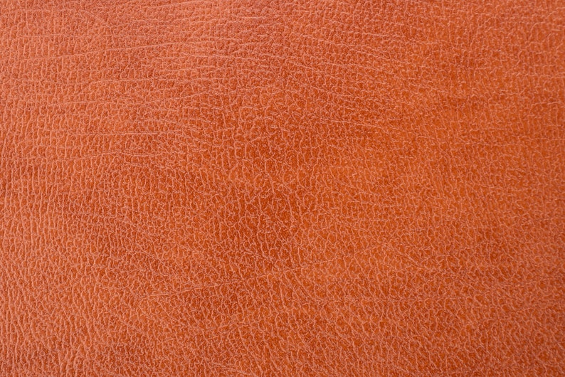 Puede incluir: Primer plano de una superficie de cuero texturizado, marr&oacute;n anaranjado. El cuero tiene un patr&oacute;n fino y agrietado, creando una apariencia detallada y t&aacute;ctil. El color es un tono c&aacute;lido y terroso, lo que sugiere un material natural.