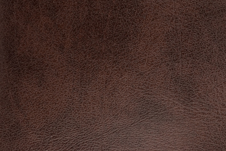 Puede incluir: Primer plano de una superficie de cuero marr&oacute;n oscuro texturizado. El cuero tiene un grano natural y un color rico y c&aacute;lido, ideal para tapicer&iacute;a o artesan&iacute;a.