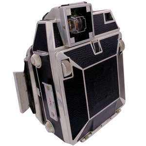 Puede incluir: Una cámara vintage plateada y negra con una cubierta de cuero. La cámara tiene un visor en la parte superior y una serie de diales y botones en el lateral.