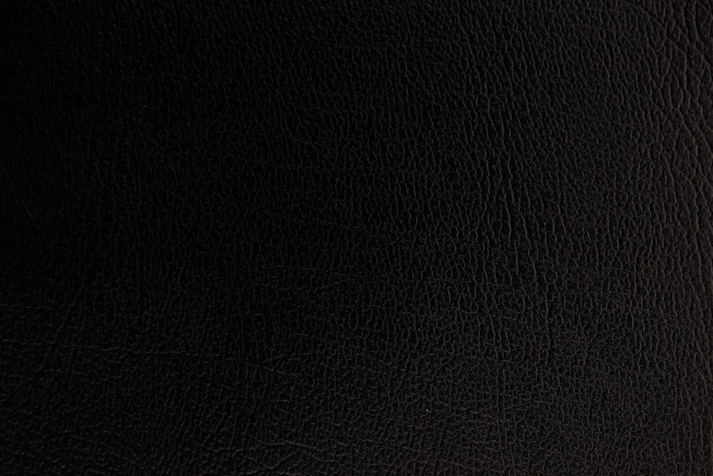 Puede incluir: Primer plano de una textura de cuero negro. La superficie tiene un grano fino y granulado, con sutiles variaciones de tono y sombra. La apariencia general es oscura y rica, lo que sugiere un material duradero.