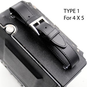 May include: Black leather camera strap with a silver buckle. The strap is attached to a black camera case. The text "TYPE 1 For 4 X 5" is printed on a white background.