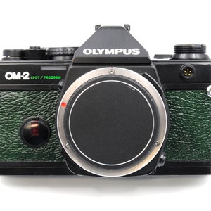 May include: A black and green Olympus OM-2 Spot/Program 35mm film camera with a silver lens ring.