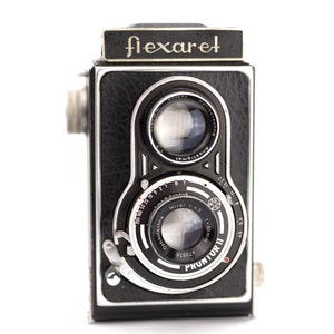 May include: A black and silver vintage Flexaret camera with a Prontor II shutter and a Mirar 1:4.5 lens. The camera has a black leather covering and a silver metal trim.