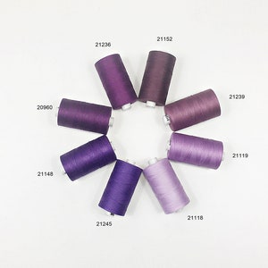 May include: A collection of eight spools of thread in various shades of purple, arranged in a circle. The spools are labeled with numbers, including 20960, 21148, 21245, 21118, 21119, 21239, 21152, and 21236.