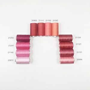 May include: A collection of 11 spools of thread in various shades of pink and red. The spools are arranged in a semi-circle with the numbers 20863, 21111, 21150, 21242, 21154, 21121, 21151, 20994, 21250, 21241, and 21149 printed on the spools.