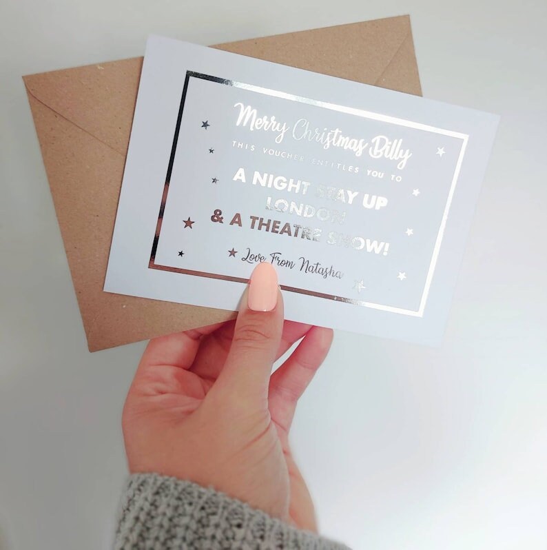 May include: A white card with silver foil lettering that reads "Merry Christmas Billy. This voucher entitles you to a night stay up London & a theatre show! Love from Natasha."